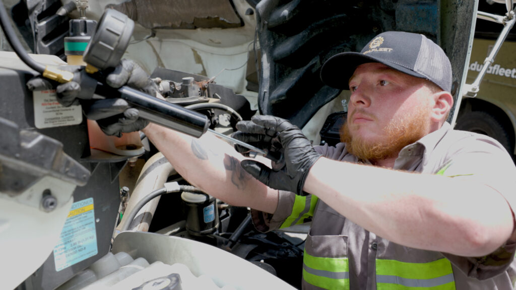 Fleet mechanic performing maintenance on a commercial truck engine.