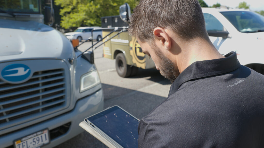 Man using a tablet to inspect a commercial truck in a parking lot.